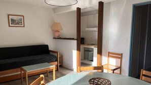 A room with a round table, two wooden chairs, a black sofa, a lamp, and a kitchen area visible through an open door. - 4th floor, jacuzzi, hammam, tv, ski locker, 40m², Peyragudes (Germ)