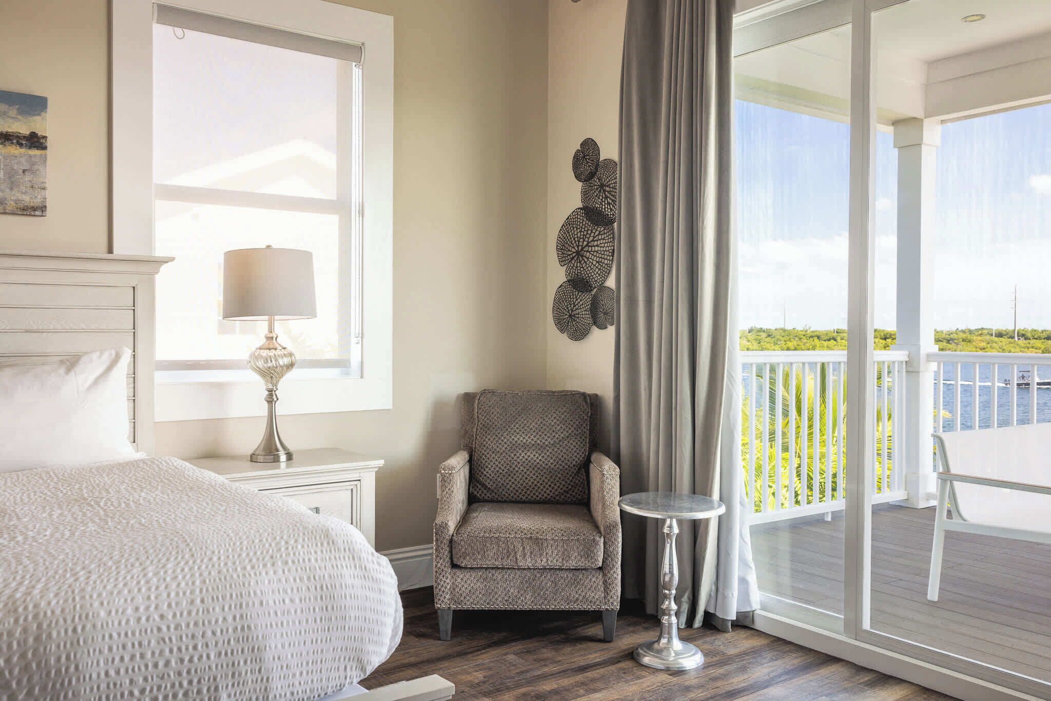 Une chambre à coucher avec un lit, une chaise, une petite table et une vue sur l’extérieur.