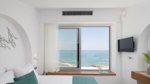 Un dormitorio con una cama grande, vistas al mar, un televisor y una mesita junto a la ventana.