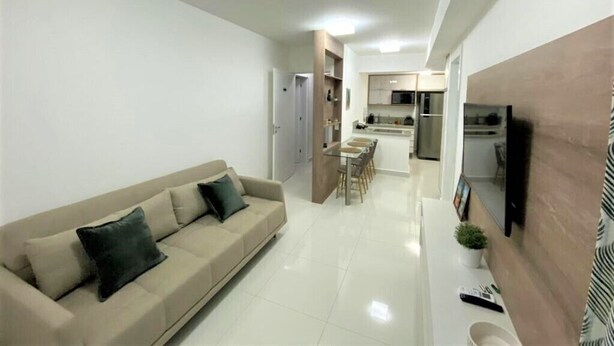 A modern living room with a sofa, a dining area, and a kitchen in the background. - In Mare praia de Cotovelo por Carpediem (Parnamirim)