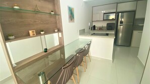 A modern kitchen with a glass dining table, wooden chairs, and a stainless steel refrigerator. - In Mare praia de Cotovelo por Carpediem (Parnamirim)
