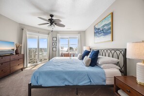 A bedroom with a bed, a ceiling fan, a TV, and a view of the ocean through large windows. - Beachfront House - Dogs OK - Pool, Near Golf (Murrells Inlet)