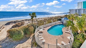 A pool area with a curved design, surrounded by a wooden deck and white lounge chairs. - "Mermaid's Delight" Oceanfront Beach House w/pool (Murrells Inlet)