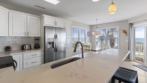 A modern kitchen with white cabinets, a stainless steel refrigerator, a marble countertop, and pendant lighting. - "Mermaid's Delight" Oceanfront Beach House w/pool (Murrells Inlet)