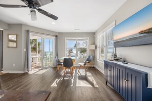 A modern living room with a dining area, large windows, and a ceiling fan. - Beachfront House - Dogs OK - Pool, Near Golf (Murrells Inlet)