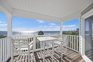 A covered outdoor area with a table and chairs, overlooking a beach with the ocean and a clear sky. - Beachfront House - Dogs OK - Pool, Near Golf (Murrells Inlet)
