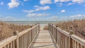 A wooden boardwalk leading to a beach with a clear sky and ocean in the background. - "Mermaid's Delight" Oceanfront Beach House w/pool (Murrells Inlet)