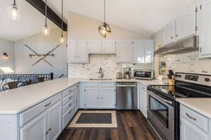 Une cuisine moderne avec des meubles blancs, un îlot central, des appareils en acier inoxydable et des luminaires suspendus.