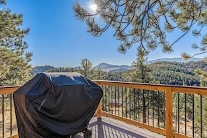 Un barbecue abrité sur une terrasse en bois, offrant une vue sur une chaîne de montagnes boisées.