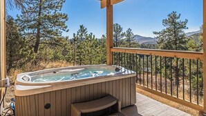 A hot tub on a wooden deck with a view of pine trees and mountains.