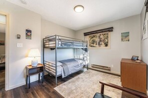 A bunk bed room with a desk, lamp, and a small cabinet.