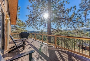 A wooden deck with a grill, a bench, and a view of a pine tree and distant mountains. - Hot tub & Sleep 6 at The Colorado Cabin (Bailey)