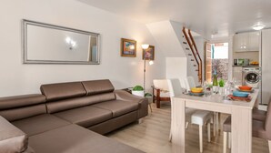 A modern living room with a brown leather sofa, a dining table with chairs, a kitchen area with cabinets and appliances, and a staircase leading to an upper level. - "Piece of Ocean by Mea Substantia" (Playa de la Américas)