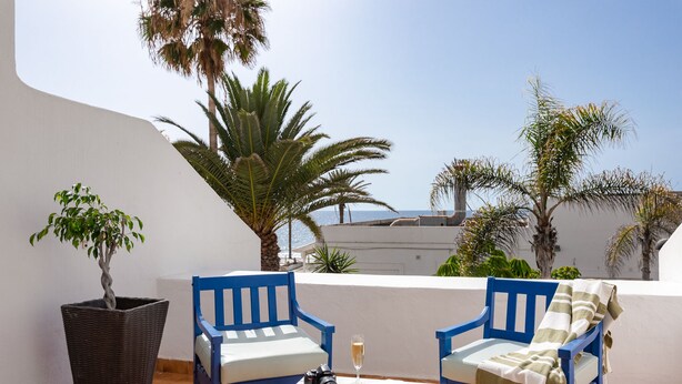 A terrace with two blue chairs, a table with a camera and a glass of champagne, and a potted plant. - "Piece of Ocean by Mea Substantia" (Playa de la Américas)