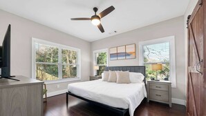 Ein Schlafzimmer mit Bett, Schreibtisch, Deckenventilator und großen Fenstern.