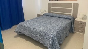 Ein Schlafzimmer mit einem Bett, einem Nachttisch, einer Lampe und einem Bild von einer Strandlandschaft.