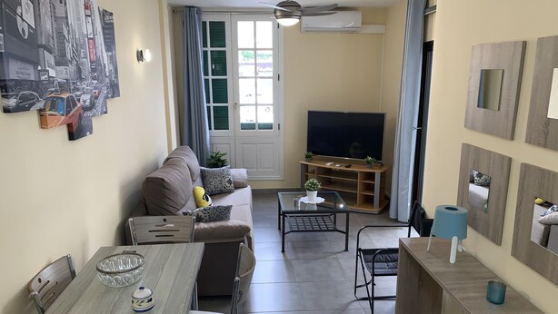 Ein Wohnzimmer mit einer Couch, einem Fernseher, einem Esstisch, Stühlen und einem Deckenventilator.