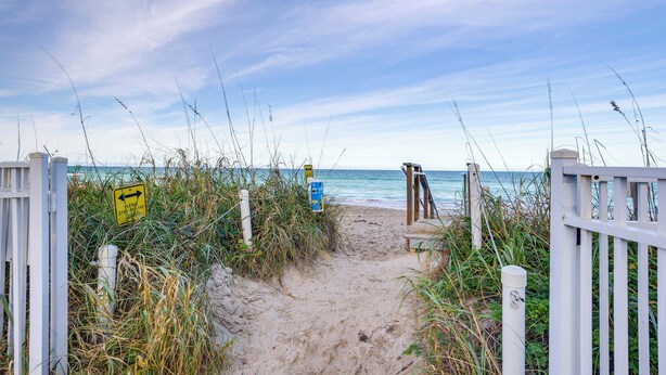 A sandy beach path with a wooden bench and a white fence. - Nettles Island Jensen Beach Home: Walk to Ocean! (Jensen Beach)