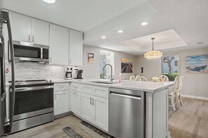 A modern kitchen with stainless steel appliances, a central island, and a dining area with chairs. - Luxury Villa, w/ Patio Steps to Beach Hilton Head (Hilton Head Island)