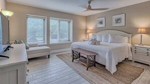 A bedroom with a bed, bedside tables, a desk, a bench, and two windows.