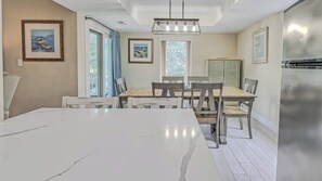A modern dining area with a marble table, wooden chairs, and a chandelier.
