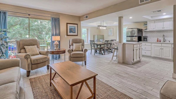 A spacious living room with a dining area, kitchen, and large windows.