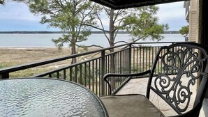Un balcón con vistas a un lago, barandilla metálica y una mesa de vidrio.