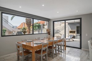 A dining area with a wooden table set for six, large windows, and a view of a residential area.