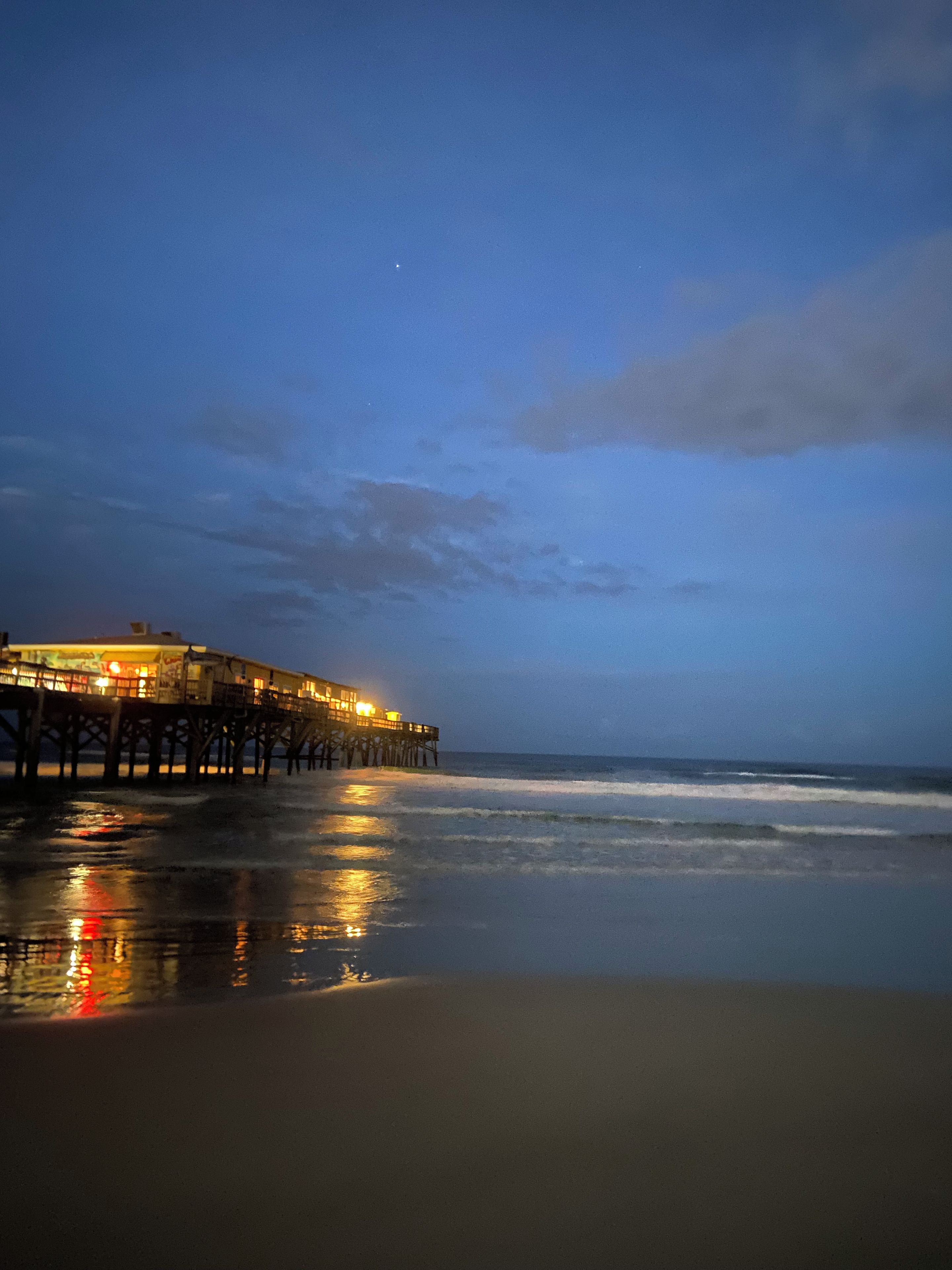 A pier extending into the water with a building on it, and the beach in the foreground.