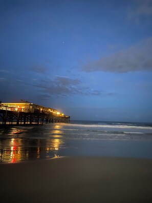 A pier extending into the water with a building on it, and the beach in the foreground. - Oceanfront, non-drive beach, heated pool, sport courts, gym (Daytona Beach Shores)