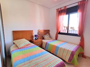 A bedroom with two beds, a wooden headboard, a nightstand, a radio, and a window with curtains.