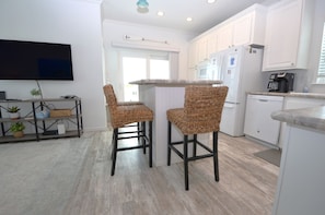 A modern kitchen with white cabinets, a built-in oven, and a coffee maker. There are two wicker chairs at a small table. - 44ft Seawall at Sportsman's Paradise (Summerland Key)