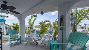 A covered outdoor seating area with turquoise chairs and tables, a ceiling fan, and a view of palm trees and buildings. - 44ft Seawall at Sportsman's Paradise (Summerland Key)