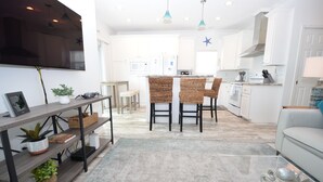 A modern kitchen with white cabinets, a central island, and a dining area with wicker chairs. - 44ft Seawall at Sportsman's Paradise (Summerland Key)