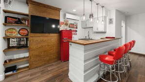 A kitchen with a wooden cabinet, a red refrigerator, and a bar area with red stools.