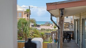 A balcony with a view of the beach, wooden deck, and outdoor furniture.