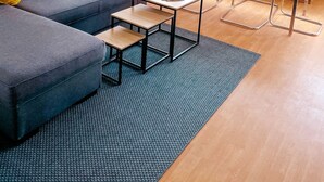 Una sala de estar moderna con un sofá gris, una pequeña mesa de centro de madera y un comedor con sillas transparentes y una mesa de vidrio.