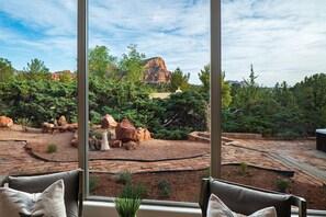 A view from a window overlooking a landscaped garden with a rock formation, trees, and a patio area.