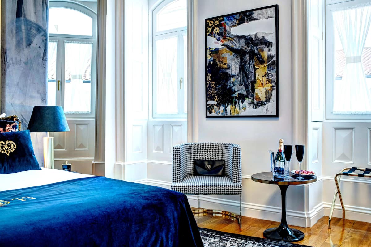 Una habitación de hotel con una cama grande, una silla, una mesa con bebidas y un cuadro en la pared.