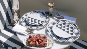 A balcony with a table set for two, featuring striped chairs and geometric plates. - 1877 Estrela Palace Hotel (Aveiro)