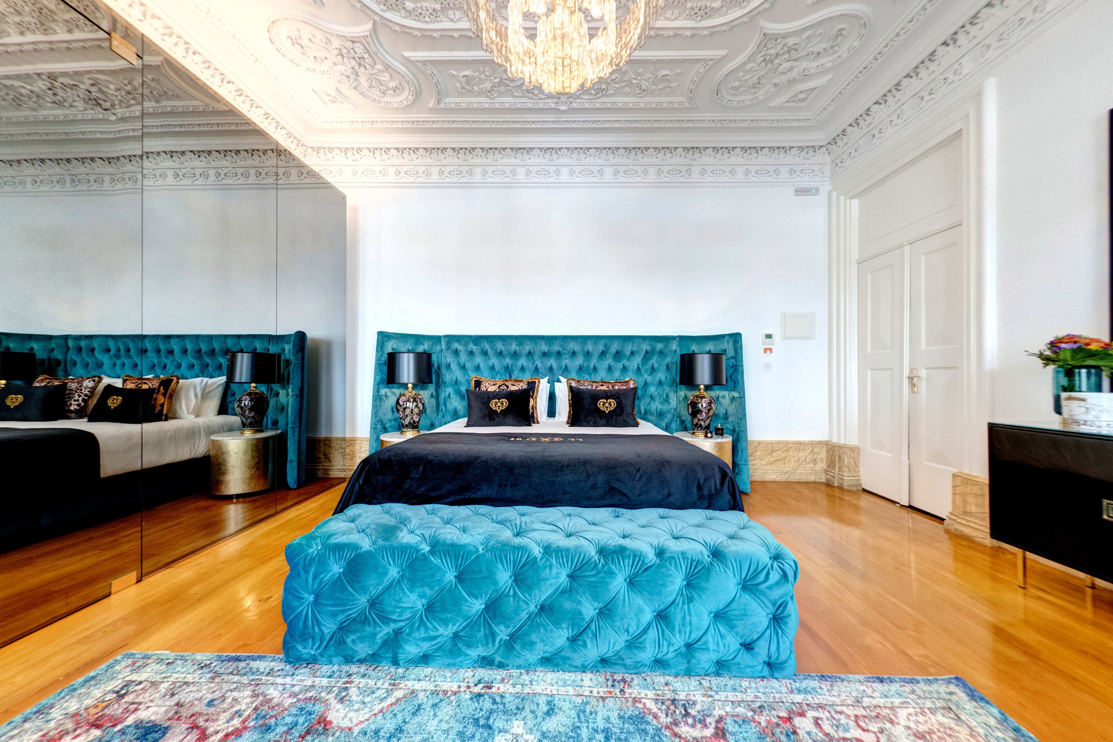 Um quarto luxuoso com uma cama grande, duas mesas de cabeceira, um candelabro e piso de madeira.