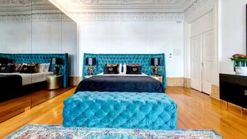Um quarto luxuoso com uma cama grande, duas mesas de cabeceira, um candelabro e piso de madeira.