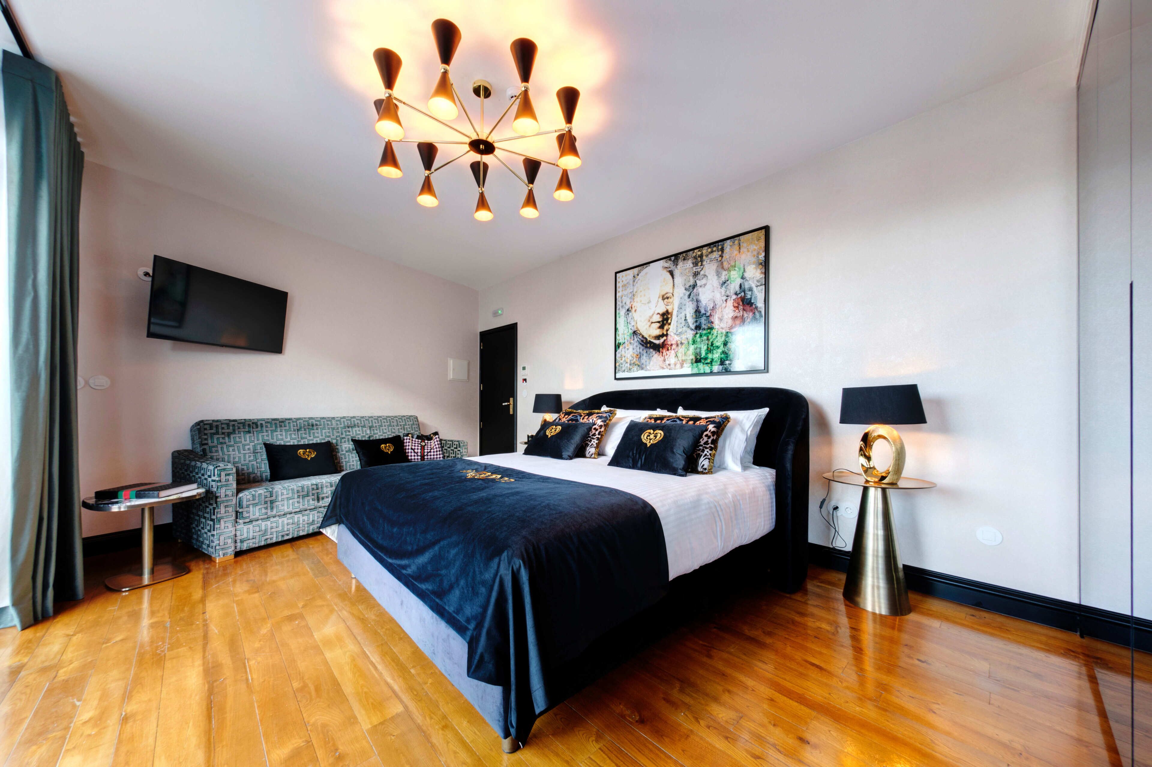 A modern hotel room with a large bed, a sofa, a TV, and a unique chandelier.