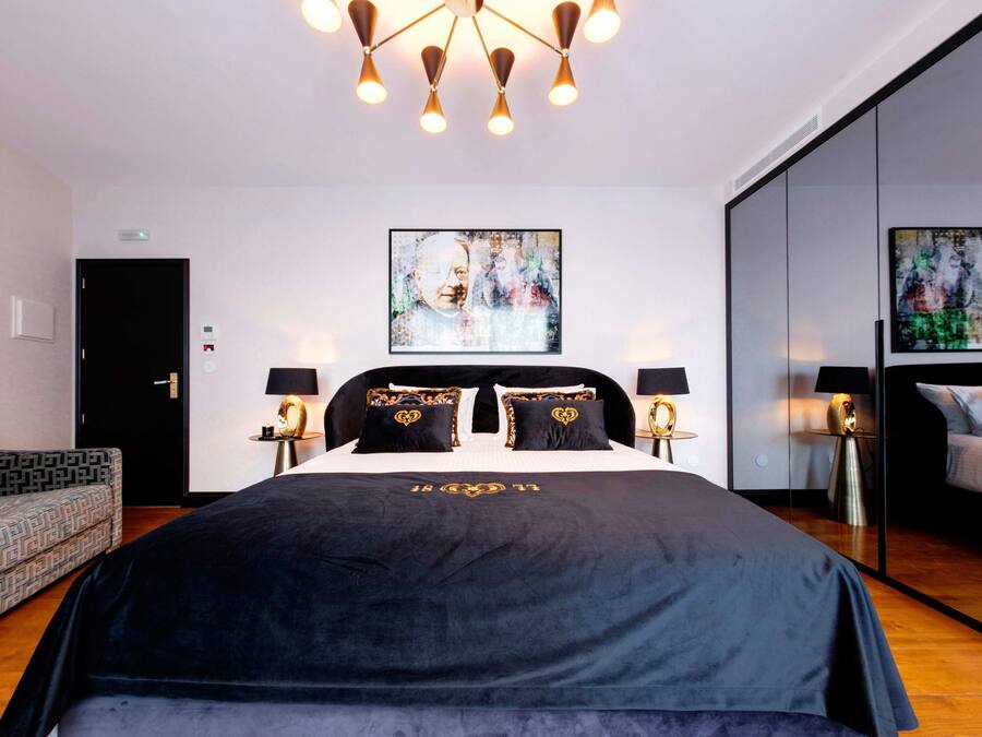 Een moderne hotelkamer met een groot bed, twee nachtkastjes met lampen, een gestreept fauteuil en abstracte kunst aan de wanden.