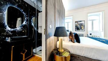 Quarto de hotel com toucador em mármore, cama com cobre-cama azul e um quadro na parede.