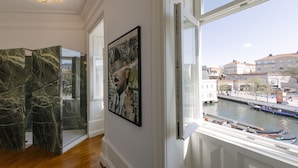 A room with a large window overlooking a canal with boats, a marble floor, and a framed artwork on the wall. - 1877 Estrela Palace Hotel (Aveiro)