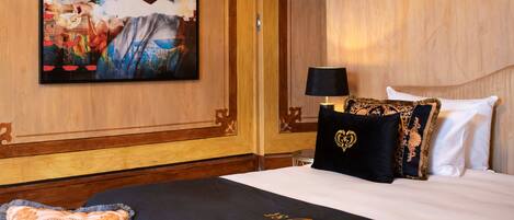 Une chambre d’hôtel avec un grand tableau abstrait au mur, un lit avec une literie blanche et noire, et un décor mural en panneaux de bois.