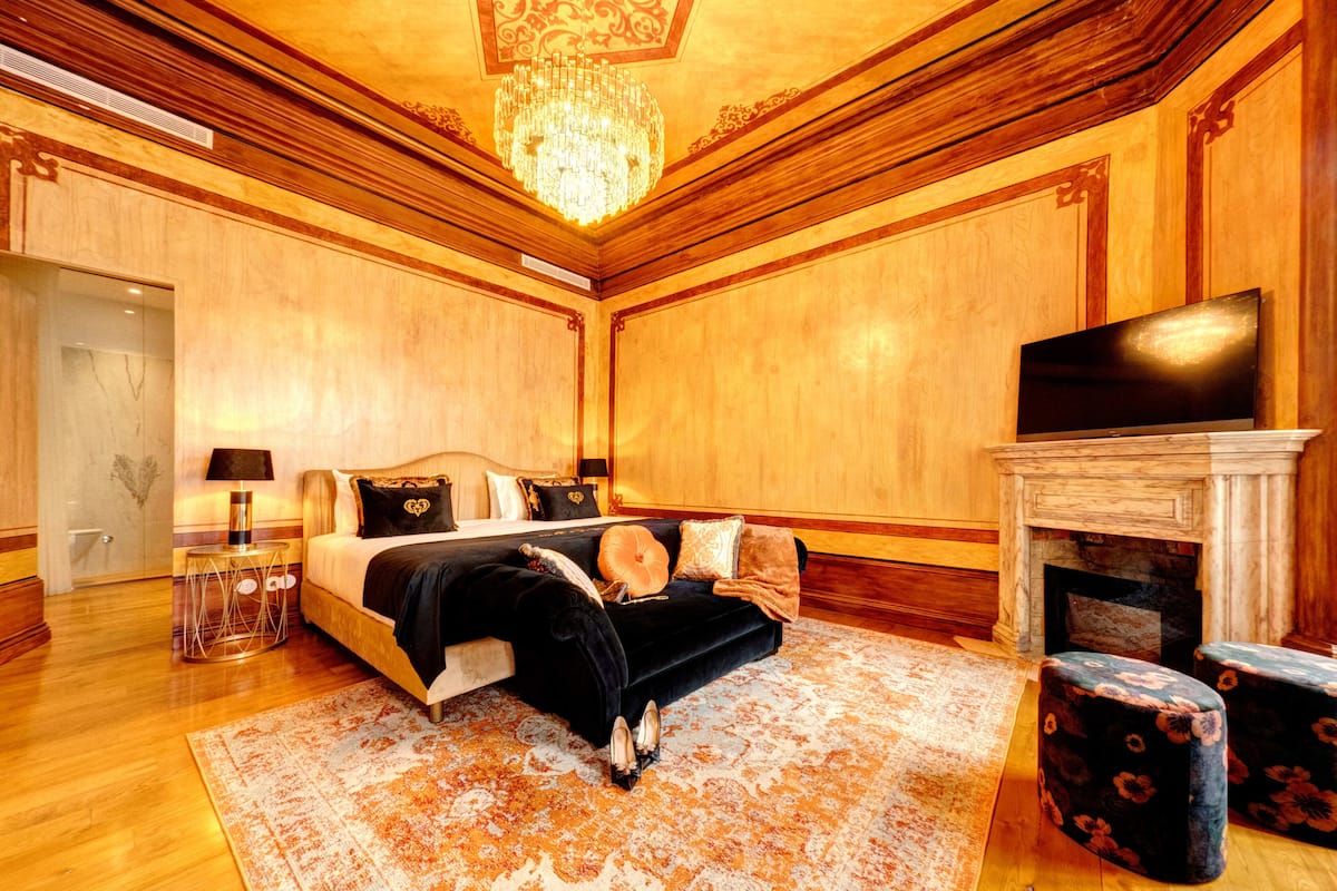 Un dormitorio lujoso con una cama grande, televisión, chimenea y candelabro.