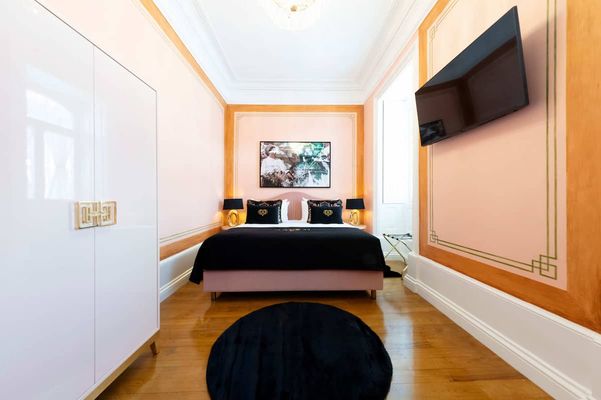 Un dormitorio con cama, lámparas de noche, televisión montada en la pared y un cuadro.