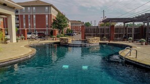 A swimming pool with a stone feature, surrounded by a wooden deck and potted plants. - Welcome to Rising Tide! (Tuscaloosa)